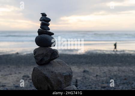 Zen stacking stones during sunset on the beach covered with rocks washed ashore at a low tide after Tonga's volcanic eruption. Stock Photo