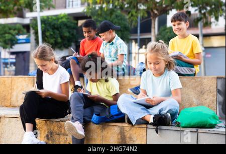 Tweenagers studying outside school, writing in workbooks Stock Photo