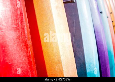 Row of many vibrant multicolor colorful red blue purple yellow kayak surfing boards surfboards boats in rental shop store in Florida abstract closeup Stock Photo