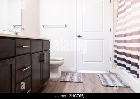 Empty bathroom interior nobody in new construction modern luxury apartment home house and white toilet with rug, door cabinets and shower bath curtain Stock Photo