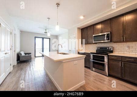 Empty kitchen and living room open plan modern apartment with large big island microwave oven and window balcony by sofa couch in luxury house home Stock Photo