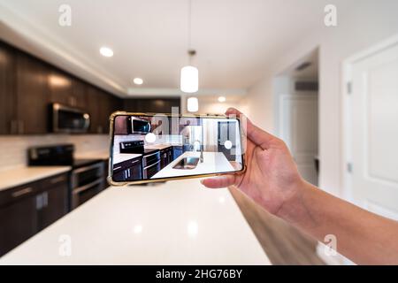 Hand photographing house apartment kitchen island room for sale or rent with phone smartphone closeup point of view in modern luxury condo home with b Stock Photo