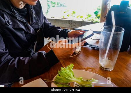 the businessman in the restaurant is using a cellphone.  he was wearing a black jacket.  photo taken at noon Stock Photo