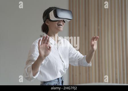 Impressed amazed female office worker using VR glasses while working in augmented reality world Stock Photo