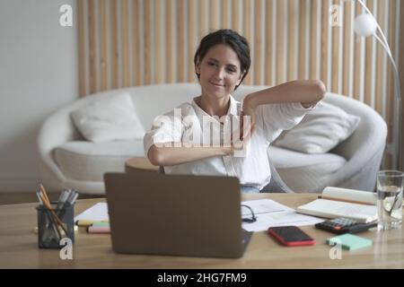 Positive business woman doing hands stretching exercises while listening to training lectures online Stock Photo