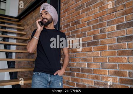 Indian man in beige turban standing on stairs and talking on the phone Stock Photo