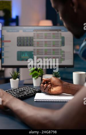 Close up of entrepreneur analyzing numbers of stock market trade writing global profit on notebook in living room. Freelancer man working remote from home thinking to invest in crypto currency Stock Photo