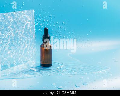 A bottle with a pipette, a cosmetic product, splashes and drops of water on a blue background Stock Photo