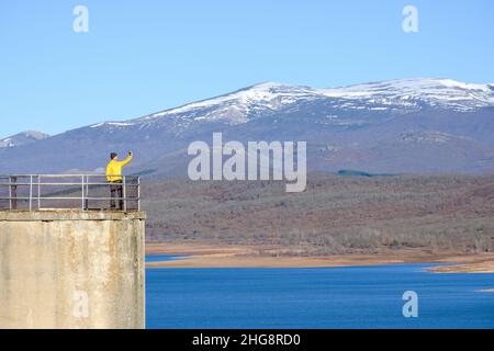 a man takes a selfie with his smartphone from a lookout point over the lake Stock Photo