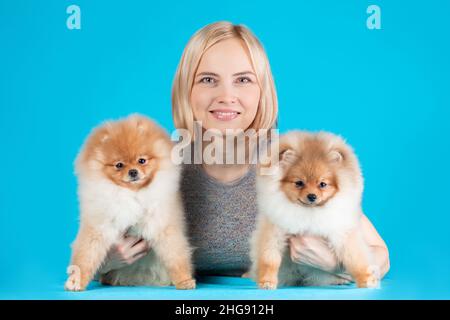 Smiling pretty woman holding two cute puppies of pomeranian spitz breed dog. Owner with her friends pets. Stock Photo