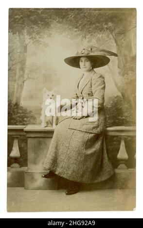 Original Titanic / late Edwardian era studio portrait postcard of attractive lady in large hat wearing a fashionable jacket and skirt, with terrier dog, dates to circa 1911 studio of Woodwards, Guernsey.