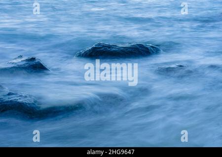 Long exposure smooth ocean wave moving into rock. Stock Photo