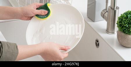 Close up of woman housewife is doing the dishes at home kitchen by using wash sponge and dishwashing. Stock Photo