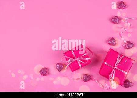 Overhead view of wrapped gift boxes with heart shaped ornaments on a pink background Stock Photo