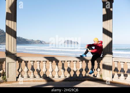 Young latin man relaxing and using his phone while sitting at seaside Stock Photo