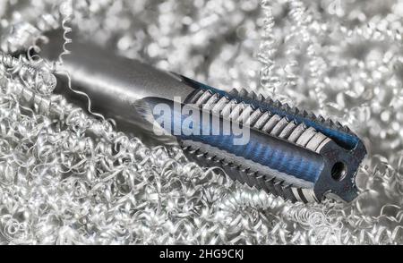 Spiral point straight fluted tap in a metal swarf heap. Beautiful steel tapping tool detail. Metric screw thread drill bit for creating threaded holes. Stock Photo