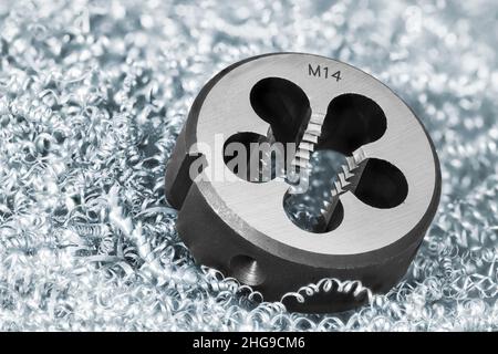 Close-up of steel solid threading die on background of metal swarf heap. Round metric tool to precise cutting external thread on cylindric rod or bolt. Stock Photo