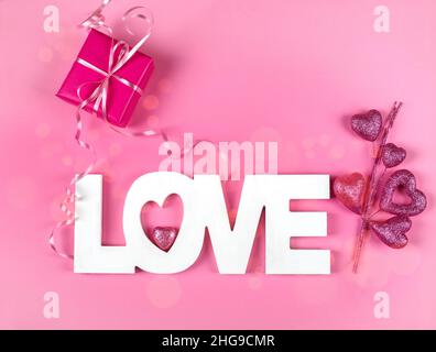 Wrapped gift box with the word Love and pink heart ornament on a pink background Stock Photo