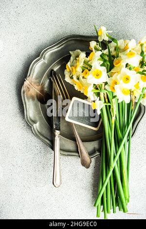 Overhead view of a bunch of narcissus flowers on a pewter plate with cutlery and a chalk nameboard Stock Photo