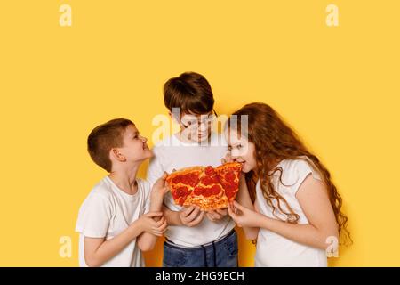 Children eating pepperony pizza on yellow background. Stock Photo