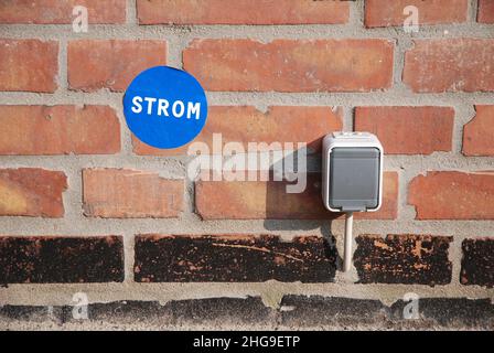 Power socket outdoor on a brick house wall with blue energy sticker Stock Photo