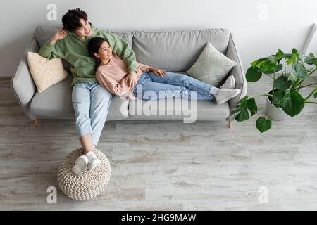 Happy relaxed millennial Asian man and woman cuddling on couch in living room, top view Stock Photo