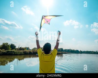 young man is standing on terrace of floating house and starting to fly bright kite in the sky, photo from back Stock Photo