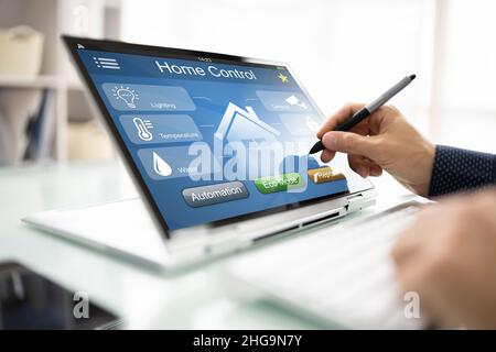 Person's Hand Using Home Control System On Digital Laptop Stock Photo