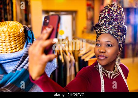 tanzanian woman with snake print turban over hear working in fabrics shop selfie taking on phone camera Stock Photo