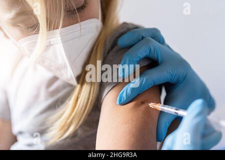 Close up hands of a nurse giving a little blonde girl first dose of Covid Vaccine in hospital. Authorized, Approved, Trial, Safe, Available, Back to s Stock Photo
