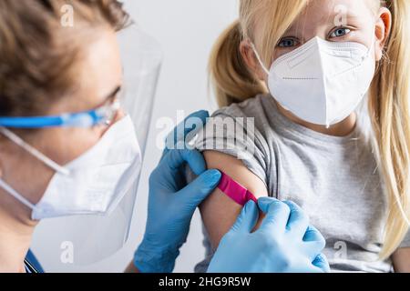 healthcare worker with protective gloves putting adhesive bandage on a arm from a blonde girl after receiving a vaccination shot for covid-19 coronavi Stock Photo