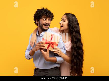 Happy indian man got present from his loving girlfriend and smiling to each other while his woman cuddling him from back Stock Photo