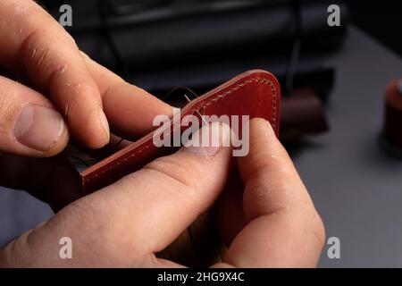 Making leather wallets. The hands of the master sew a leather product. Stock Photo