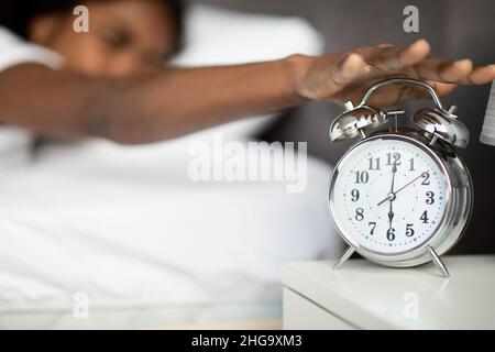 Black woman laying in bed, turning off alarm on bedside Stock Photo