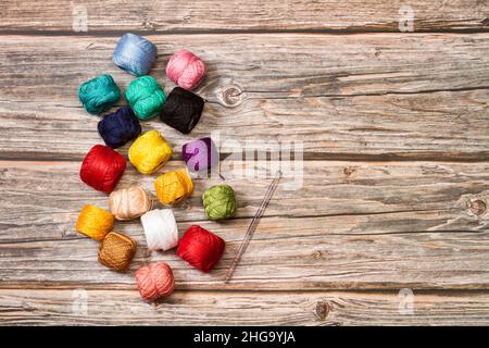 Colored yarn spools and a crochet needle on a wooden background with copy space Stock Photo