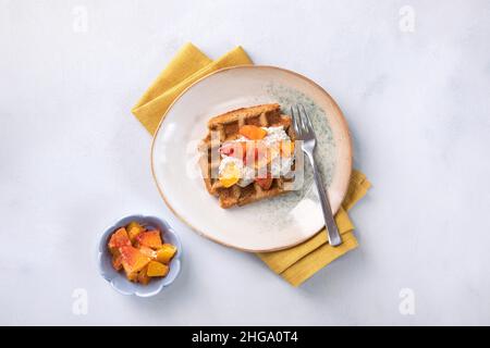 Fresh made waffles with pudding and oranges on bright neutral background. Healthy dessert, tasty homemade breakfast. Vegan, gluten free waffles. Stock Photo