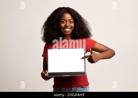 Check This Website. Cheerful Black Woman Pointing At Laptop With Blank Screen Stock Photo