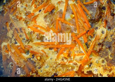 Meat with carrot is cooked in cauldron on fire. Step by step cooking of Pilaf. Stock Photo