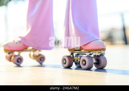 close up photo of legs woman in bell-bottomed trousers with pink pastel color roller skates outdoors in sunny day Stock Photo