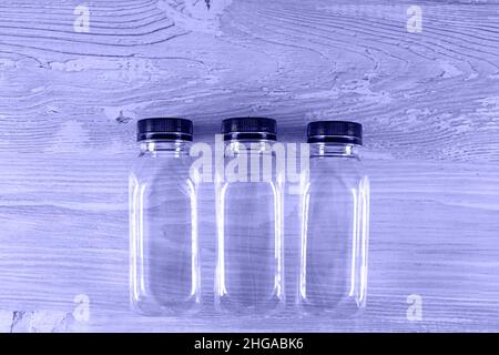 Three plastic transparent empty bottles with a black cap on a wooden table. There is a place for your logo. Very Peri toned image. copy space Stock Photo