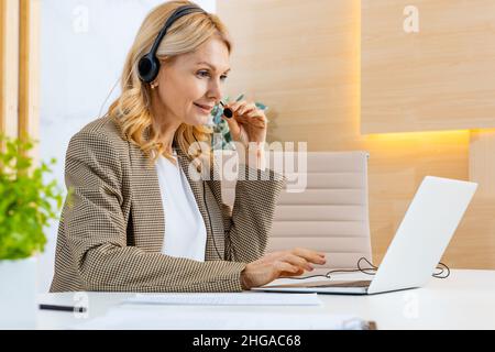 Businesswoman with elegant suit sitting at computer desk in the office and joining in a video conference - Mature adult woman working at laptop and te Stock Photo