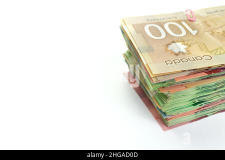 High Angle View of Large Stack of Canadian Banknotes on a White Background. Top bill is 100 one hundred and the bills are various dollar values. Stock Photo