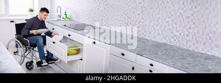 Young Happy Man Sitting In Wheelchair Arranging Plates In Drawer Stock Photo