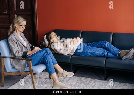 The psychotherapist listens attentively to the story of the patient lying on the couch. Stock Photo
