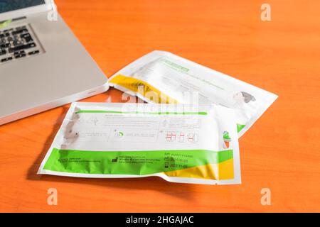 Seville. Seville, Spain. 28 December 2021. Several Covid-19 antigen self-test kits on a wooden table next to a laptop. Antigen self-testing is increas Stock Photo