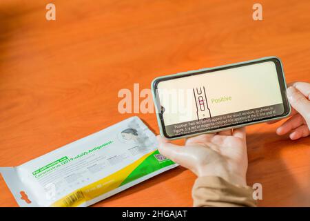 Seville, Spain. 28 December 2021. Detail of a woman's hands holding a smartphone, with a Covid19 self-test kit on a wooden table, watching a video exp Stock Photo