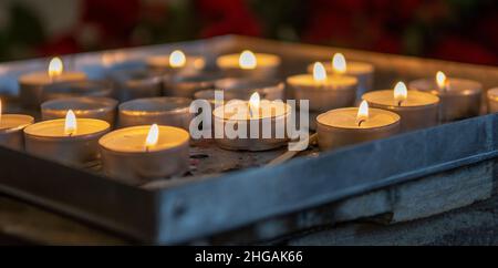 Burning prayer candles inside a catholic church. Lit tea lights. Selective focus. Stock Photo