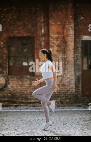 Pretty young woman warming before running in the urban environment Stock Photo