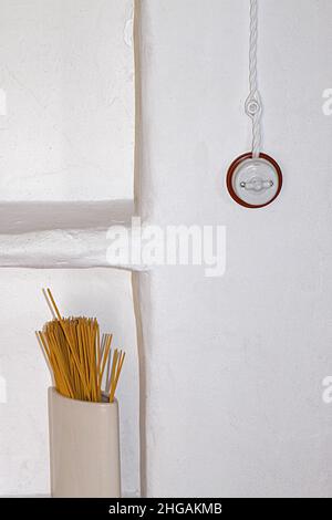 Spaghetti noodles in white container in front of white wall with old-fashioned light switch, Spain Stock Photo