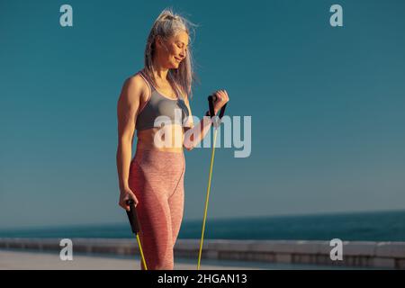 Strong woman in sportswear exercising on sports site, using fitness resistance bands Stock Photo
